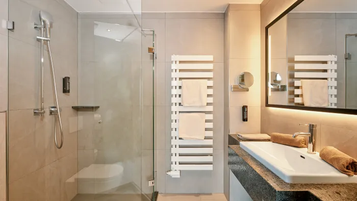 Modernes Hotelbad mit begehbarer Dusche, großem Spiegel und Waschbecken mit Granitplatte